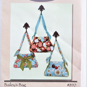 May include: A sewing pattern for a small bag called "Bailey's Bag" by Cotton Way. The pattern shows three different bags with floral and geometric prints in shades of blue, green, red, and brown.