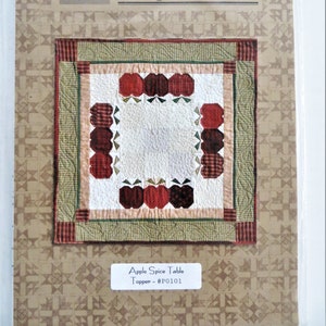 May include: A quilting pattern for an apple spice table topper, featuring a red, green, and white patchwork design with the text "Apple Spice Table Topper - #P0101".