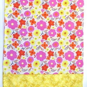 Puede incluir: Una tela blanca con un patrón repetitivo de flores rosas, naranjas y amarillas. La tela tiene un borde amarillo en la parte inferior.