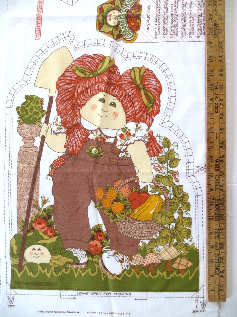Puede incluir: Un patr&oacute;n de tela con una ni&ntilde;a de pelo rojo que lleva un mono y sostiene una cesta de verduras. La ni&ntilde;a est&aacute; de pie en un jard&iacute;n con una rana, flores y setas. El patr&oacute;n incluye instrucciones para hacer una mu&ntilde;eca Cabbage Patch Kid. El texto del patr&oacute;n dice "Cabbage Patch Kids" y "Dejar abierto para rellenar".