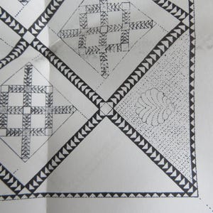 May include: Close-up of a white surface with a repeating geometric pattern in black. The design features diamond shapes with intricate internal patterns and borders of triangles. A dotted floral design is in one of the diamond shapes.