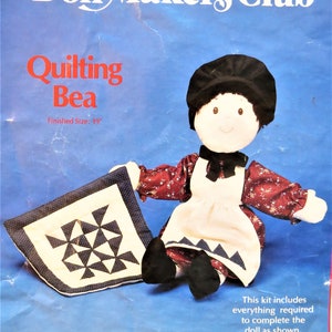 May include: A doll making kit featuring a doll named "Quilting Bea" with a finished size of 19 inches. The doll is wearing a white apron and a red and white patterned dress. The kit includes everything needed to complete the doll as shown. The kit and stuffing are made in the USA.