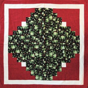 May include: A red and white quilt with a black and green fabric square in the center. The fabric square is a pattern of Christmas trees and snowflakes.