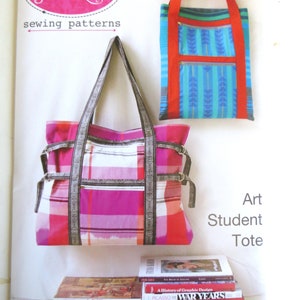 May include: A pink and white plaid tote bag with black straps and a gray trim. The bag is hanging on a white wall with a stack of art books underneath. The text "Art Student Tote" is printed on the wall.