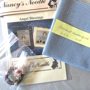 May include: A cross stitch kit with a blue fabric, a pattern for "Angel Blessings" with two designs, and a small bag of embellishments. The fabric is 12 x 16 inches and 16 count.