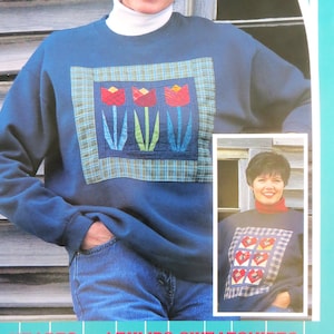 May include: A navy blue sweatshirt with a floral design featuring three red tulips with green stems and leaves. The design is framed by a blue and green plaid pattern. The text "HEARTS and TULIPS SWEATSHIRTS" is at the bottom.