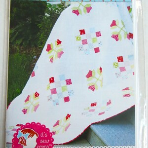 May include: A quilt pattern called "Georgia" featuring a white quilt with pink, red, and green floral designs. The quilt is on a set of stairs with a green bush in the background. The pattern is from "It's Sew Emma" patterns.
