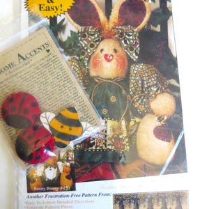 May include: A craft pattern for a honey bunny and bumble bee friends. The pattern includes a picture of a cute bunny doll wearing a green dress and a bumble bee doll with a heart-shaped pouch. The pattern is from Happy Hollow Designs and is titled "Quick & Easy!"