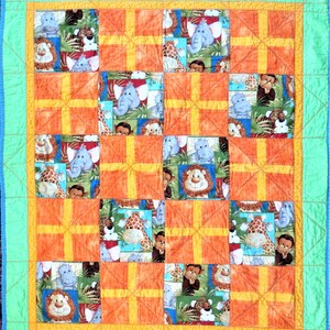 Puede incluir: Una colcha de retazos con temática de animales de la selva. La colcha está hecha de tela naranja, amarilla y azul con imágenes de elefantes, jirafas, leones y monos. La colcha está bordeada con un borde azul claro.