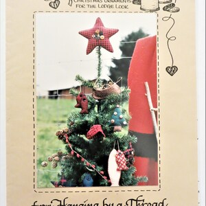 May include: A Christmas ornament pattern booklet titled "Reelin' in the Holidays" with a red and black plaid star ornament on a Christmas tree. The booklet is from "Hanging by a Thread by Connie's Calicos, Too" and includes the address 6100 NE 131st Ave Vancouver, WA 98682 and phone number (206) 944-6131. Copyright 1993.