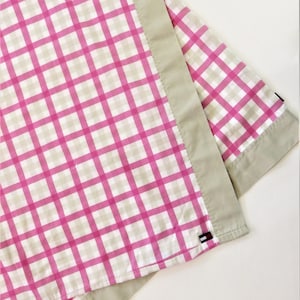 Puede incluir: Una tela a cuadros rosa y blanca con un borde beige. La tela tiene un pequeño logotipo bordado en la esquina inferior derecha.