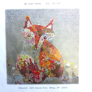 May include: A colorful fabric art piece titled "Freida" by Laura Heine, featuring a fox design. The artwork is 35 x 35 inches and showcases a detailed patchwork of floral and patterned fabrics in shades of red, orange, and green against a textured gray background.