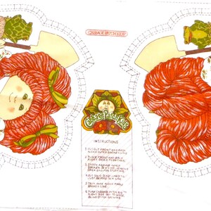 Puede incluir: Un panel de tela con dos im&aacute;genes de una ni&ntilde;a pelirroja con un mono y sosteniendo una pala. La ni&ntilde;a est&aacute; rodeada de follaje verde y flores. El panel incluye el texto "Country Girl Charm" e instrucciones para hacer una mu&ntilde;eca.