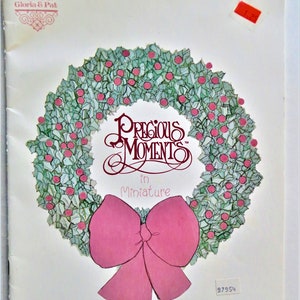 May include: A book cover featuring a green holly wreath with red berries and a pink bow. The title is "Precious Moments in Miniature".