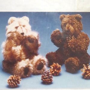 May include: Two plush teddy bears, one brown and one white, are sitting on a blue background.  The bears are holding pine cones in their paws.  There are several pine cones scattered around the bears.