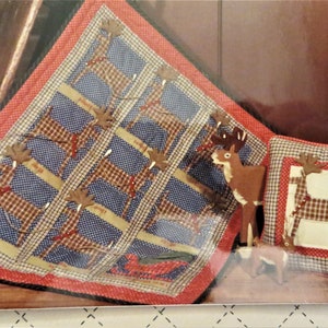May include: A red and blue plaid quilt with a pattern of brown reindeer. The quilt is surrounded by a red border. There is a smaller pillow with a similar design in the background.
