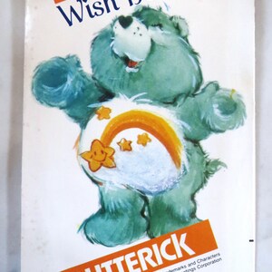 May include: Wish Bear Care Bear sewing pattern from Butterick. The pattern features a blue bear with a rainbow and stars on its belly. The pattern number is 6234.