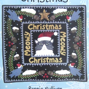 May include: A square fabric wall hanging featuring a central black cat wearing a red plaid Santa hat. The border displays pine branches, pinecones, red berries, and blue birds in Santa hats. Text reads Meowy Christmas, Bonnie Sullivan, All Through the Night.