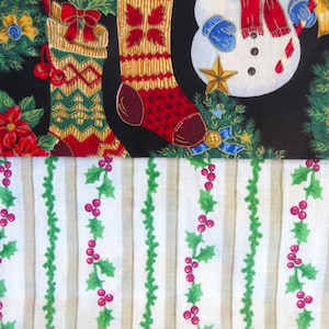 Puede incluir: Una tela negra con un muñeco de nieve, acebo y dos calcetines rojos y dorados. La tela se combina con una tela blanca con acebo verde y bayas rojas.