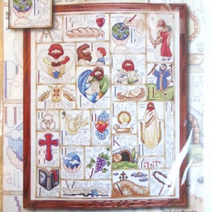 Może przedstawiać: Zestaw do haftu krzyżykowego o nazwie "Inspirational ABC" o wymiarach 40,6 x 50,8 cm po ukończeniu. Zestaw zawiera oprawiony wzór z religijnymi obrazami i tekstem, w tym słowa "Chleb Życia" i "Słowo Życia".
