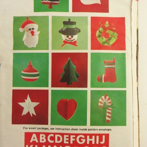 May include: A sheet of paper with a grid of 12 squares, each containing a different Christmas ornament design. The ornaments are made of felt and include a bell, a dove, Santa Claus, a snowman, a wreath, an ornament, a Christmas tree, a stocking, a star, a heart, and a candy cane. The paper also includes the alphabet in red letters.