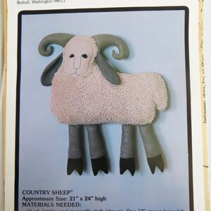 May include: A pattern for a Country Sheep, approximately 53 cm by 61 cm high. The sheep is made of beige, light brown, grey, and black felt, with a fluffy body and curved horns. The pattern includes materials needed and instructions.