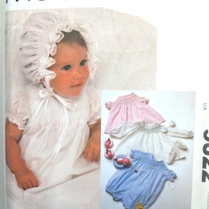 May include: A vintage McCall's sewing pattern featuring a baby in a white bonnet and dress. The pattern includes images of baby dresses and rompers in pink, white, and blue. The McCall's logo is at the top.