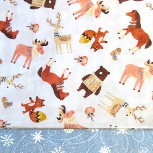 Puede incluir: Tela blanca con un patrón repetido de animales del bosque, incluyendo ciervos, zorros, búhos y caballos. La tela tiene un patrón de copo de nieve azul y blanco en la parte inferior.