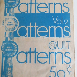 May include: A vintage blue and white pamphlet titled "23 Quilt Patterns" with the text "Vol. 2" and "50 cents" printed on the front. The pamphlet features a blue ribbon with the text "Blue Ribbon First" printed on it.