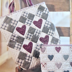May include: A quilted tote bag and a matching zippered pouch with a patchwork design featuring hearts in shades of burgundy and black. The bag has a brown handle and the pouch has a zipper closure.