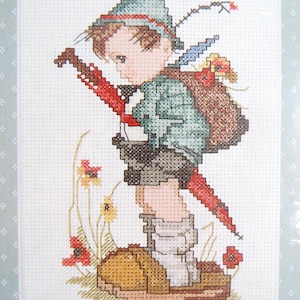 May include: Cross-stitch pattern featuring a young boy with a backpack and a red umbrella, walking through a field of red and yellow flowers. The pattern is signed "Hummel".
