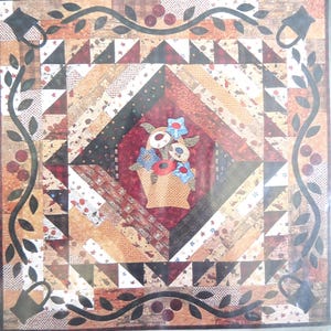 May include: A patchwork quilt with the title "Baskets & Vines" by Nancy Odom. The quilt features a central diamond design with a basket of flowers and deer. The color palette includes browns, reds, and greens.