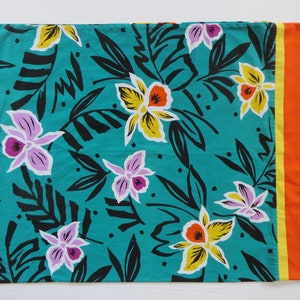 Puede incluir: Una tela turquesa con un patrón floral con flores amarillas, naranjas, rosas y blancas. La tela tiene un borde negro y un borde amarillo y naranja en el lado derecho.