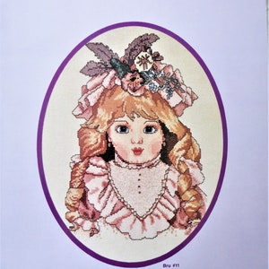May include: A counted cross stitch pattern featuring a Victorian doll with blonde hair, wearing a pink dress and a hat with flowers. The pattern is titled "...A Victorian Experience" and is from London Doll Co.