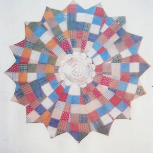 May include: A starburst-shaped patchwork quilt with a white doily at its centre. The quilt is made of fabric squares in red, blue, orange, and green, creating a vibrant, handcrafted design. The quilt's edges are pointed, giving it a unique shape.