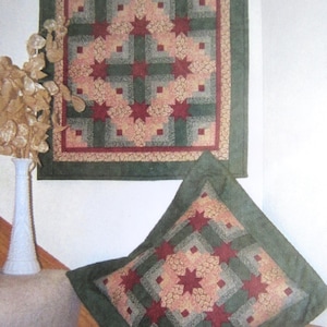 May include: A quilted wall hanging and pillow featuring a star pattern. The design incorporates red, green, and tan fabrics. The wall hanging is square, and the pillow is diamond-shaped, both with a green border. The star pattern is centered on both items.