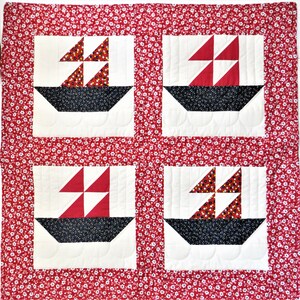 May include: A white quilt with a red border and four red, white and black sailboat blocks. The background of the quilt is a red fabric with a white floral pattern.