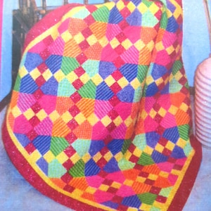 May include: A colorful patchwork quilt with a diamond pattern in shades of pink, red, yellow, green, and blue. The quilt is folded and draped over a wooden chair.