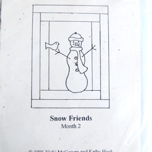 May include: A black and white line drawing of a snowman with a bird, inside a rectangular frame. The text "Folk Art Christmas Block of the Month" is at the top. Below the drawing is the text "Snow Friends Month 2".