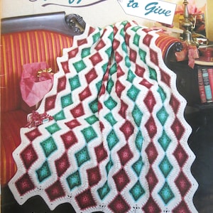 May include: A crochet pattern book titled "Afghans to Give" by Kathy Wesley. The cover features a handmade afghan with a white background and a repeating pattern of red and green diamonds. The book is from the American School of Needlework.