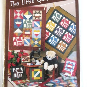 May include: A package for "The Little Quilt Collection" with images of miniature quilts. The quilts display house and geometric patterns. A teddy bear and sewing machine are also visible, indicating a quilting theme.