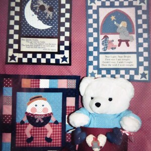 May include: A set of three framed quilted wall hangings with a patchwork design. The first features a blue and white checkered background with a white crescent moon and a poem about the moon. The second features a blue and white checkered background with a star and a poem about wishing on a star. The third features a red, white, and blue patchwork design with a whimsical character and a white teddy bear.
