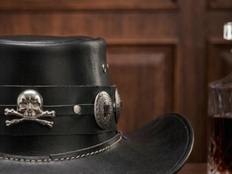 May include: Black leather cowboy hat with silver skull and crossbones emblem and decorative silver studs. The hat features a wide brim and a stitched brim edge. A stylish accessory.