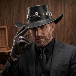 May include: A black leather hat with a wide brim, adorned with silver-toned embellishments and a skull emblem. The hat is worn with a dark suit, black gloves, and a ring. The overall aesthetic is a blend of classic and edgy styles.