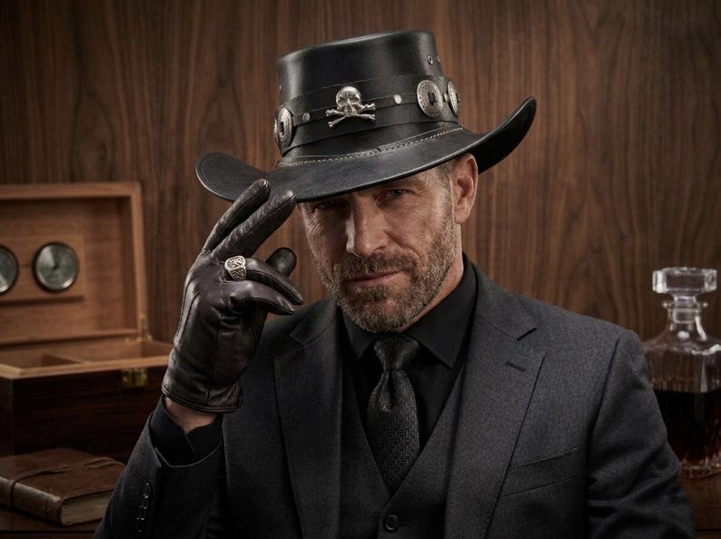 May include: A black leather hat with a wide brim, adorned with silver-toned embellishments and a skull emblem. The hat is worn with a dark suit, black gloves, and a ring. The overall aesthetic is a blend of classic and edgy styles.