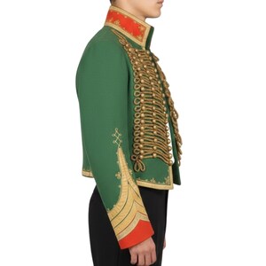 K&ouml;nnte beinhalten: Gr&uuml;ne Jacke im Milit&auml;rstil mit goldenen Seildetails und goldener Stickerei an den &Auml;rmeln. Die Jacke hat einen roten Kragen und rote Manschetten. Die Jacke ist ein Cropped-Style.