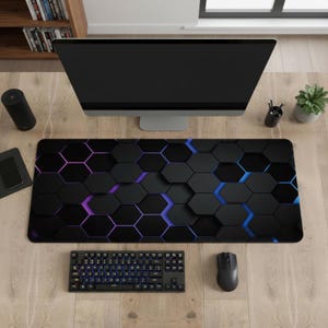 May include: Black and grey hexagonal pattern desk mat with purple and blue accents. A keyboard, mouse, and computer monitor are on the desk. The desk is made of wood.