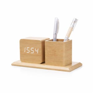 Peut inclure: Un organiseur de bureau en bois avec une horloge numérique affichant 15h54 et un porte-stylos. L'horloge et le porte-stylos sont en bois clair et reposent sur une base en bois assortie. Deux stylos sont dans le porte-stylos.