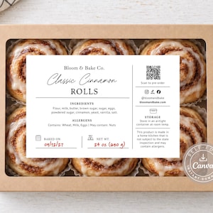 Op de afbeelding: Een rechthoekige kartonnen doos met een doorzichtig venster bevat zes kaneelbroodjes met wit glazuur. Een wit etiket bevat de tekst Bloom & Bake Co. Classic Cinnamon ROLLS, ingrediënten, allergenen, bewaarinstructies en een QR-code.