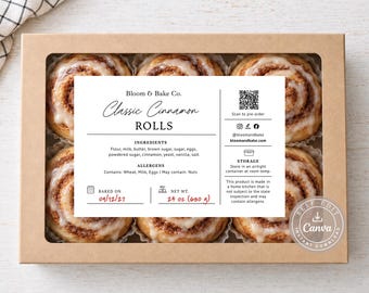 May include: A rectangular cardboard box with a clear window containing six cinnamon rolls topped with white icing. A white label features the text Bloom & Bake Co. Classic Cinnamon ROLLS, ingredients, allergens, storage instructions, and a QR code.